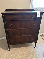 Front view of dark wooden antique highboy dresser showing five drawers and round metal ring pull handles