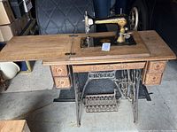 Full view of the Singer sewing machine mounted in the wooden cabinet with extended side surfaces and treadle base visible, showing overall condition and placement of the machine.