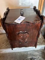 Front and side view of the antique wooden garbage can showing hinged lid, curved side handles, and carved decorative panel on front.