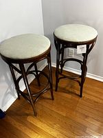 Two bentwood style stools with beige recovered seats standing on hardwood floor, showing overall shape and height.