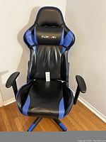 Front view of Norfan gaming chair with blue and black vinyl upholstery and padded headrest pillow with logo.