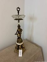 Full view of vintage standing ashtray showing brass cherub figure, marble base, and crystal dish with handle on top