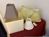 Five lamp shades in various shapes and colors displayed on a red surface.