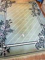 Full view of large patterned area rug in green with floral border and diagonal stripe design inside.