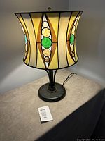 Side view of lamp showing colourful mosaic glass curved shade with art deco style patterns and dark metal base.