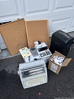 Overview of the lot on driveway showing the equipment including typewriter, printers, calculators, paper shredder, cork boards, and box of paper rolls.