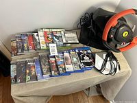 Overview of assorted Xbox 360, PlayStation 3, PlayStation 4, and Nintendo DS games along with Ferrari racing wheel and pedals showing overall lot contents.