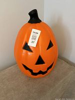 Front view of the large orange plastic pumpkin blow mold jack-o'-lantern with black facial features and stem.