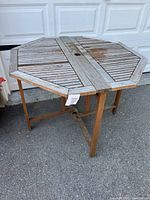 Octagonal teak folding patio table shown standing, with slatted weathered wood top and folding legs, patina visible.