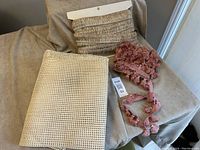 Photo showing multiple yards of dusty rose tassel trim and folded light beige cane webbing piece on a soft surface.