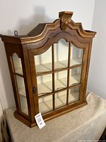 Full view of the wood and glass curio cabinet showing grid-style windowpanes and scalloped top with carved wooden crest.