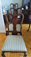 Front view of multiple mahogany dining chairs with striped fabric seats lined up.