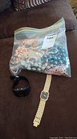 Full lot photo showing plastic bag with assorted beaded necklaces and earrings, black digital watch, and gold-tone Seiko wristwatch