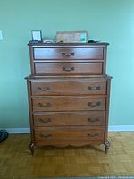 Front view of the wooden dresser showing six drawers with brass handles, medium brown finish, and curved legs.