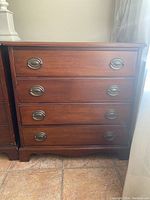 Front view of the vintage wooden dresser with four drawers and oval metal handles.