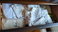 Various white linens with embroidery and lace detailing folded in drawer.