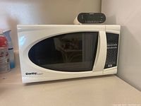 White Danby Designer microwave oven on counter with digital control panel and black tinted window, Sony digital alarm clock on top.