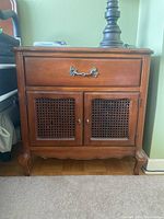 Front view of wooden night stand with drawer and two cane doors, wood finish with metal ornate drawer pull.