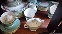 Mixed view of stacked dinner plates, side plates, cups, saucers, creamer and sugar bowl on shelf