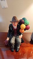 Front view of the Balloon Man figurine showing detailed facial features, colorful balloons on the back, and seated posture.