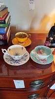 Three teacup and saucer sets on a wooden surface, overview of lot