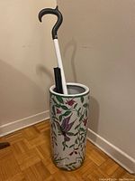 Full view of the ceramic umbrella stand with two walking canes inside, highlighting the stand's shape and painted decoration.