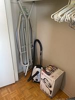 Photo of ironing board, Bissell vacuum, and box in closet space.