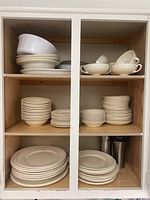 Full view of shelves with stacks of white Wedgwood dishes and bowls including teacups and saucers.