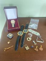 Full view of all wristwatches and mens accessories arranged on table including boxed Citizen watch, two unbranded watches, cufflinks, tie clip, pendants