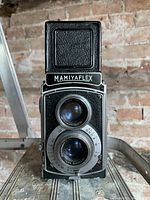 Front view of Mamiyaflex twin lens camera showing upper viewing lens and lower taking lens with aperture markings and Mamiyaflex name on hood.