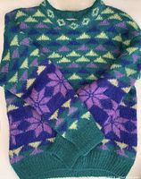 Full view of the sweater showing colorful green, purple, yellow, and cream geometric and snowflake patterns.