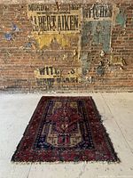Full view of antique rug laid flat on floor against brick wall