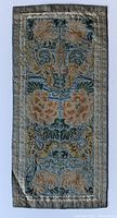 Front of the antique Chinese silk robe panel showing detailed embroidery with open flowers and foliage in gold, green, blue, and beige on a blue silk background.