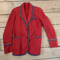 Front view of the red wool jacket with blue and gold braid trim and patch pockets on wooden floor.