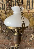 Antique ceiling lamp showing milk glass shade, brass chain and fixtures, and wood detail against a rustic background.