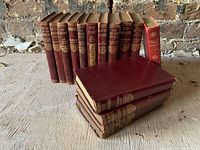 Set of 14 red leather bound antique books with gilt detailing arranged and stacked, showing their spines with titles.