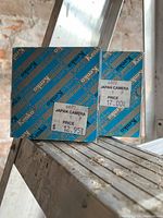 Photo of two Kenko branded filter packages with price stickers visible, placed on a wooden ladder against a brick background.