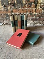Set of seven Modern Library hardcover books by Marcel Proust arranged in front of a brick wall showing cloth bindings in muted tones, some red and green with black spine labels with gold lettering.