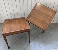 Pair of square wooden end tables with inlaid decorative border on top, tapered legs, and wood grain visible, positioned next to each other on a wooden floor.