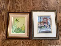 Two framed original paintings side by side on wooden floor showing full artwork and frames