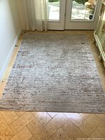 Full view of the poly area rug laid out on stone tile floor with natural light from a glass door illuminating the rug's texture and color pattern. Shows overall condition and placement.