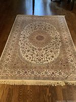 Full view of the area rug showing the intricate central medallion with floral motifs and fringe edges on hardwood floor.