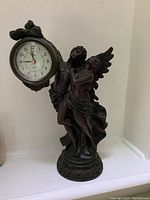 Full view of the statue clock showing two angel figures with a round clock held to the side.