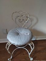 Front view of decorative metal vanity chair with round tufted cushion showing heart-shaped backrest and floral accents on legs