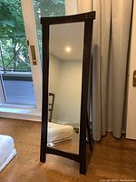 Clear image of the full length mirror standing on wooden floor, showing front view, wood frame, and part of the stand.