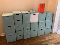 Full view of stacked blue IKEA collapsible storage boxes in various sizes against a beige wall, with orange magazine holders and one white box included.
