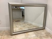Front view of large rectangular silver framed mirror placed on floor showing the full reflective surface and frame.