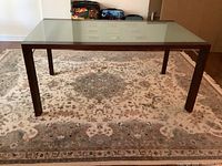 Full front view showing the glass top and wooden legs on ornate carpet.