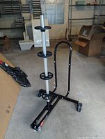 Motomaster tire storage cart shown from an angle revealing the black metal frame, vertical post with four circular tire holders, and caster wheels on a concrete floor in a garage setting.