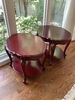 Pair of cherry finish wood end tables shown side by side near a glass window. Tables have scalloped edges and curved legs.